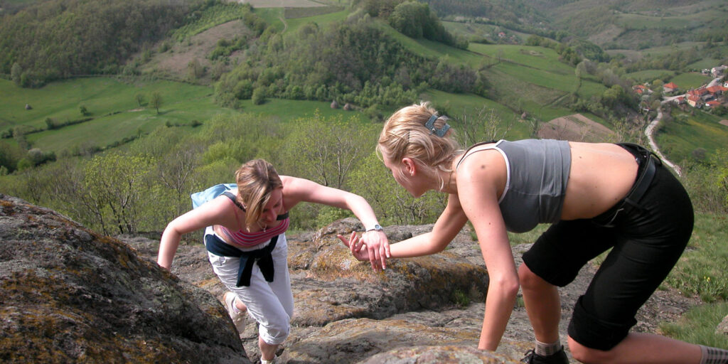 women helping each other climb a mountain